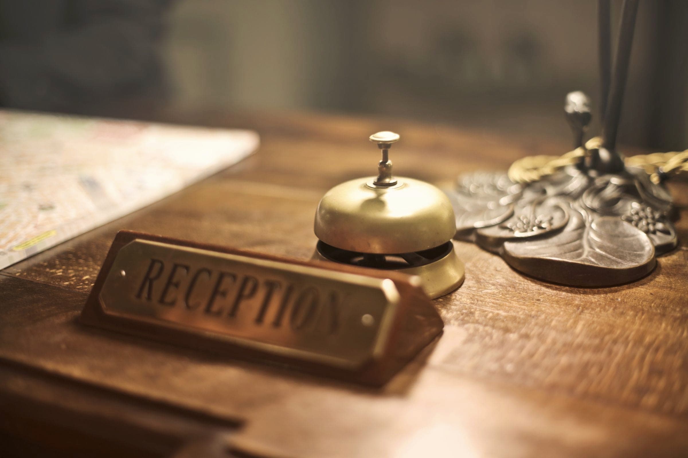 A service bell and a reception sign on a wooden hotel desk