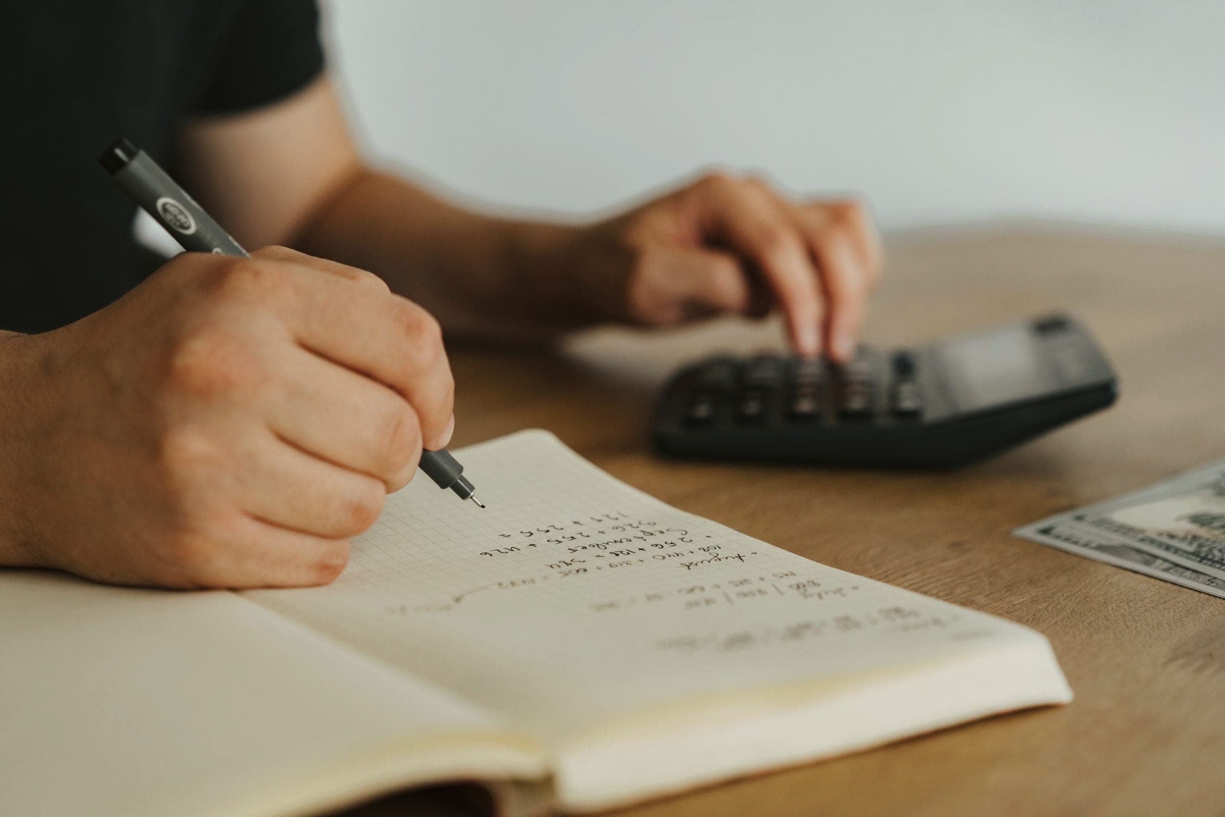 Hands writing figures in a notebook while using a calculator