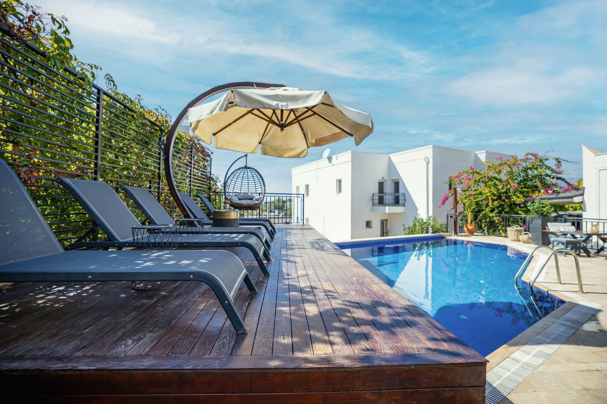 A pool with a wooden deck and sun loungers beside white buildings in Bodrum