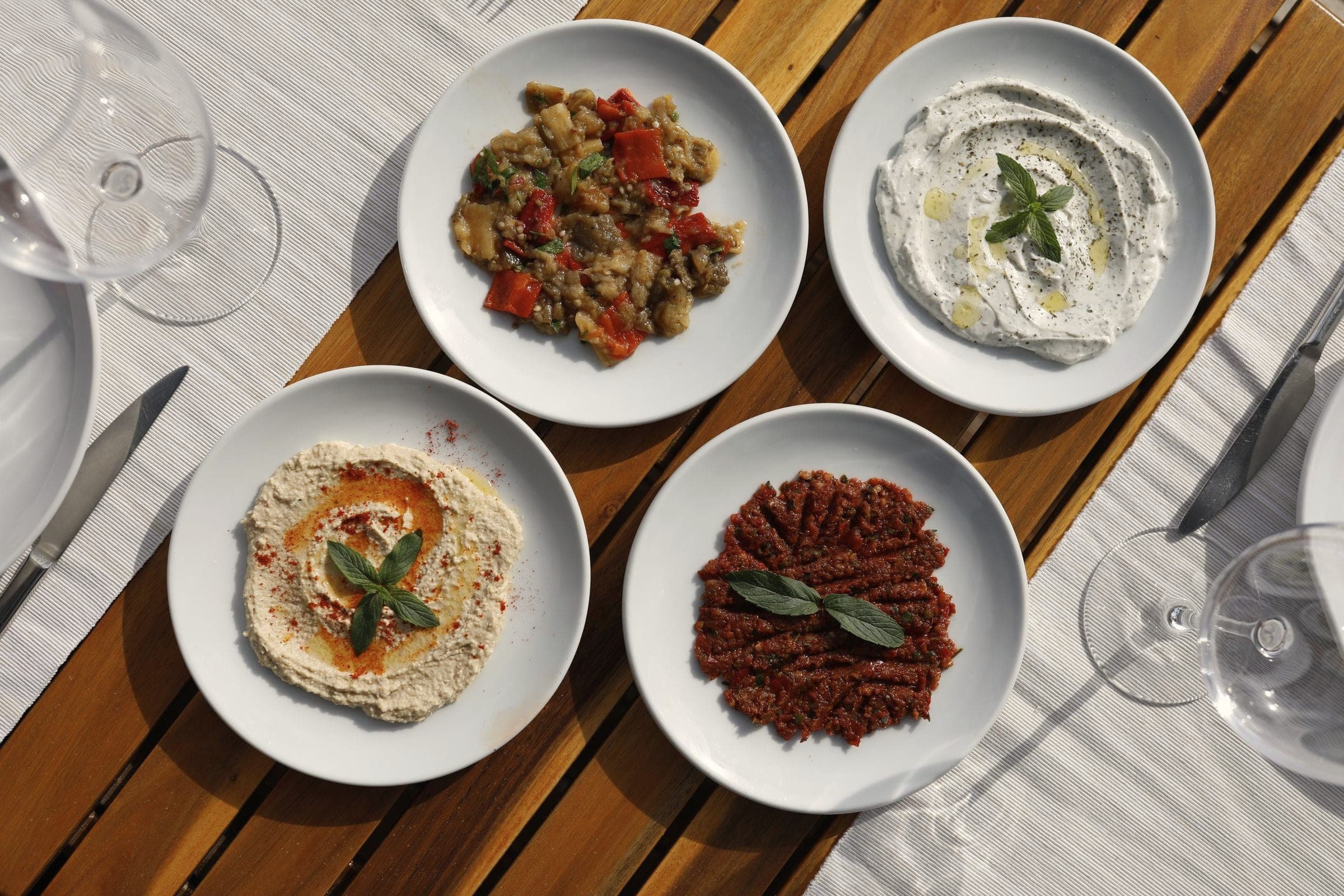 Overhead view of meze dips on white plates on a wooden table