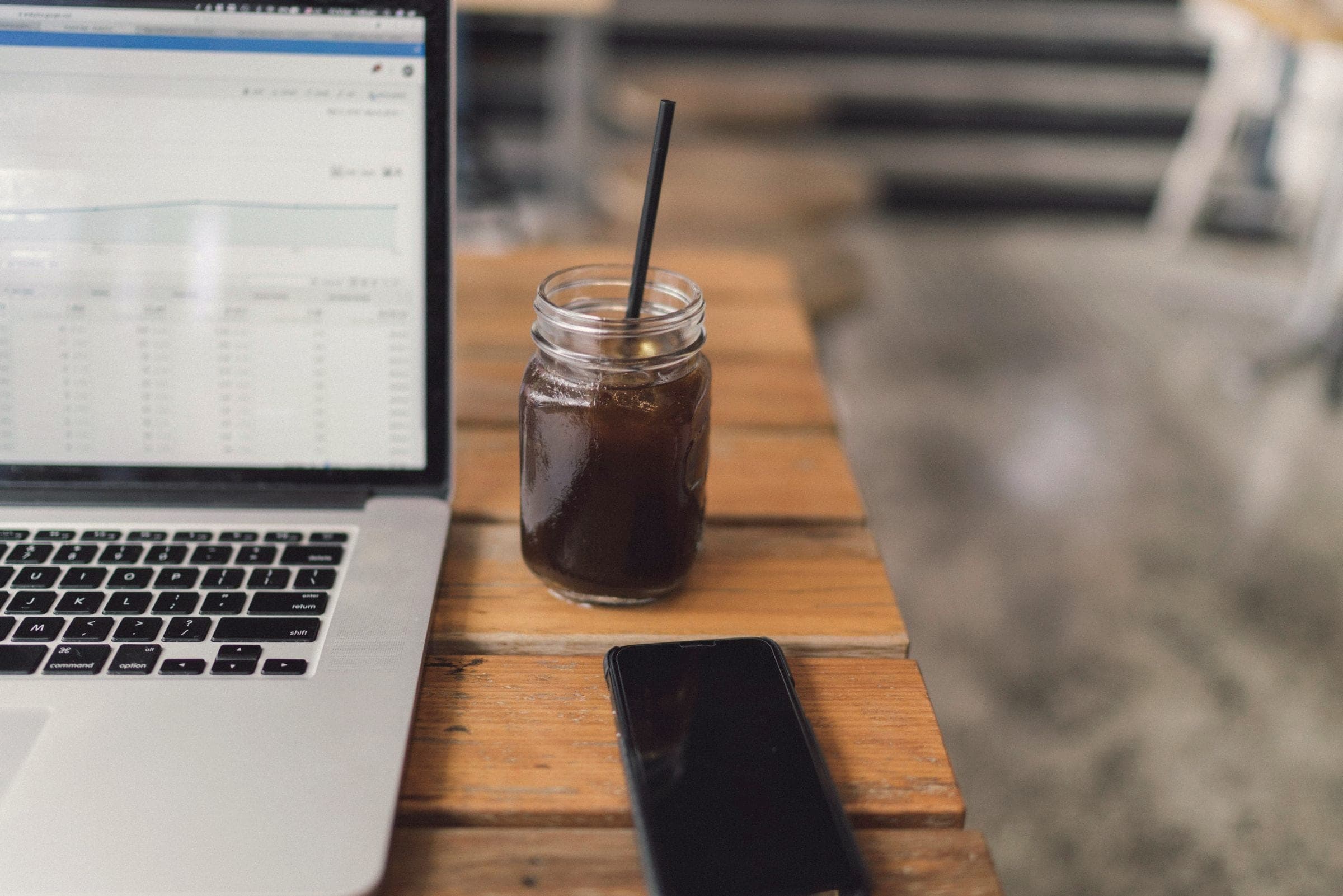 A laptop showing an analytics report on a wooden café table, with an iced coffee and a phone beside it