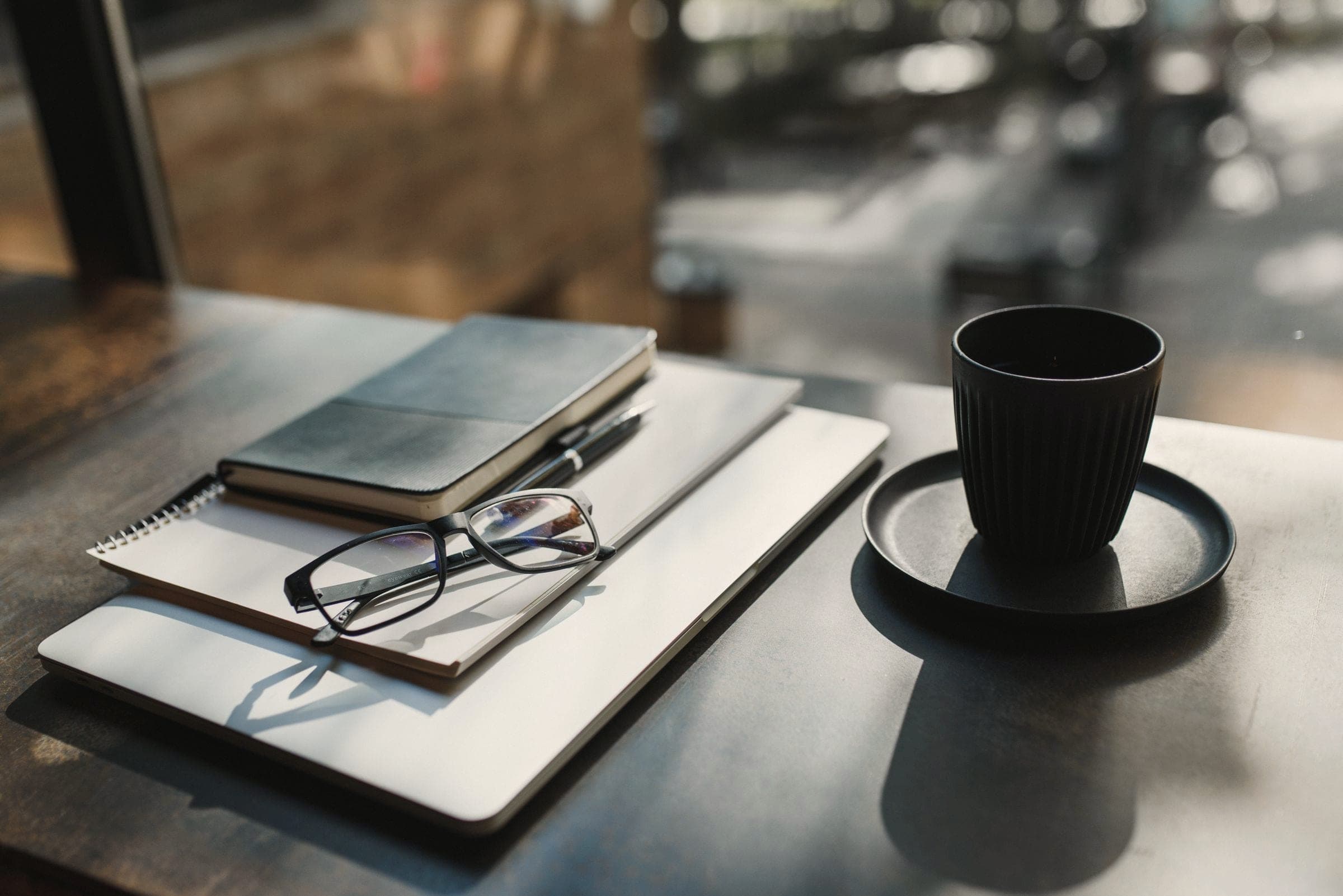 A notebook, glasses and a black cup on a dark stone-look table