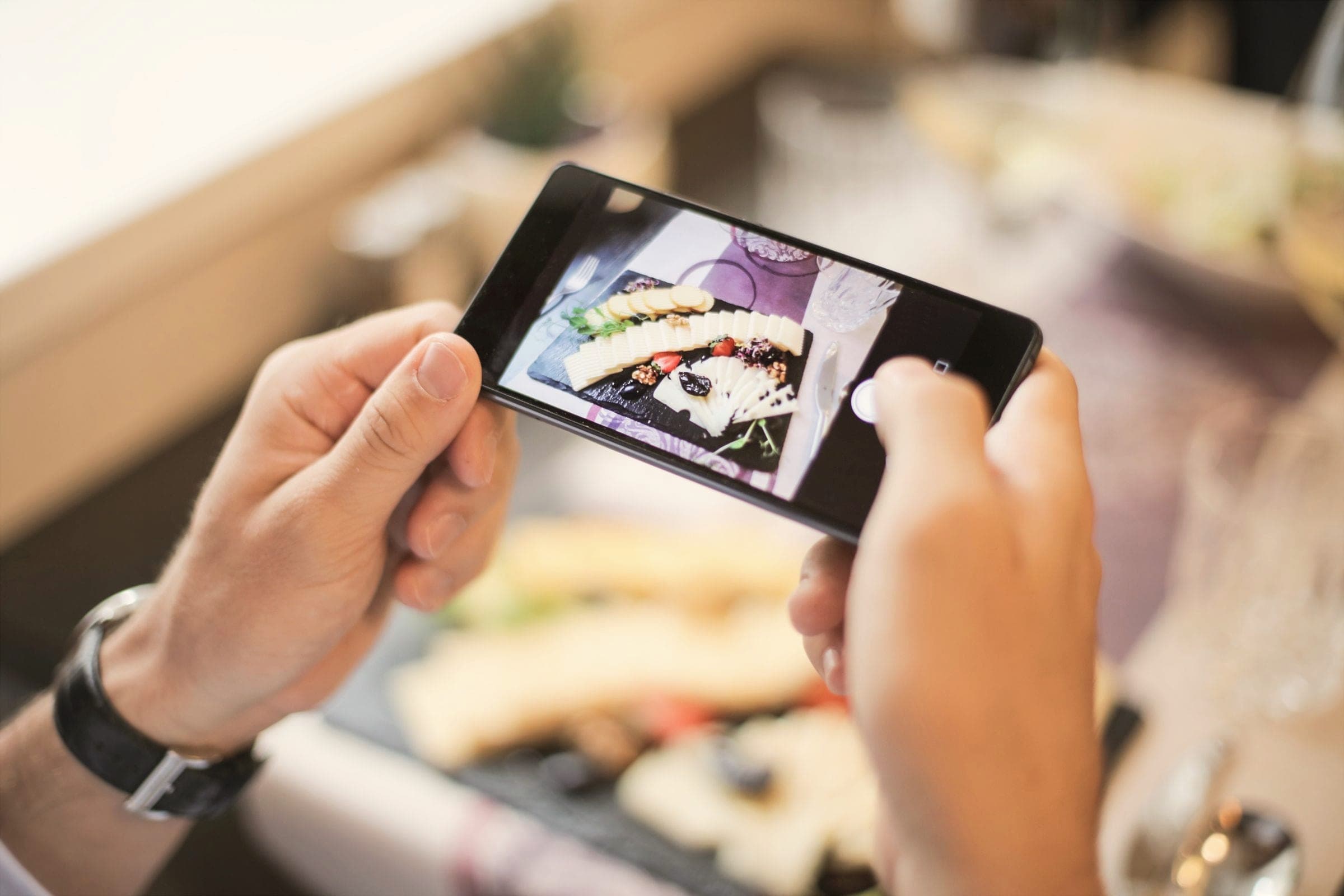 Hands holding a smartphone to photograph a plated dish on a table